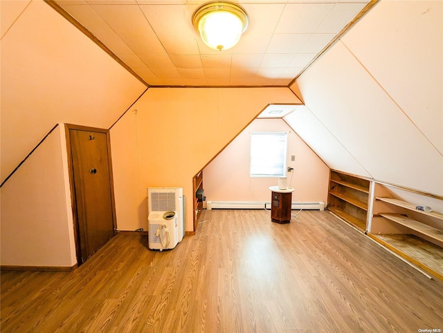 additional living space with wood-type flooring, lofted ceiling, built in shelves, and a baseboard heating unit