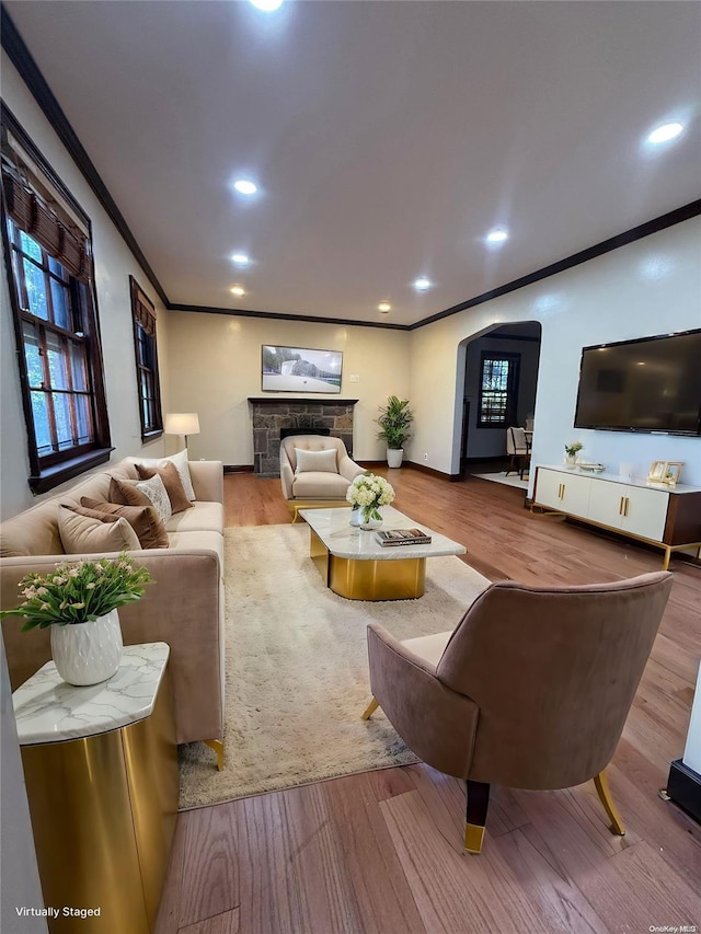 living room with hardwood / wood-style floors, a stone fireplace, and crown molding