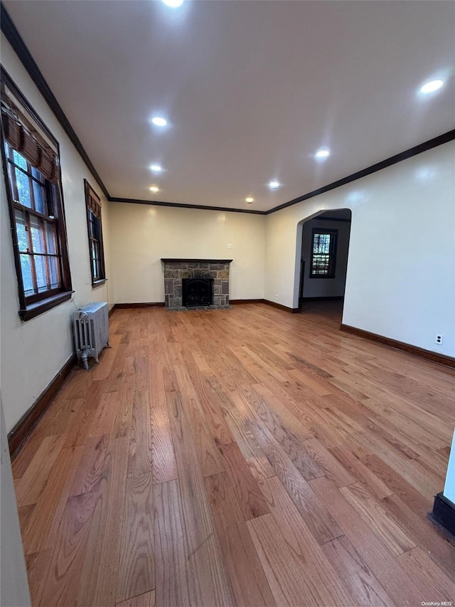 unfurnished living room featuring radiator, a fireplace, light hardwood / wood-style floors, and ornamental molding