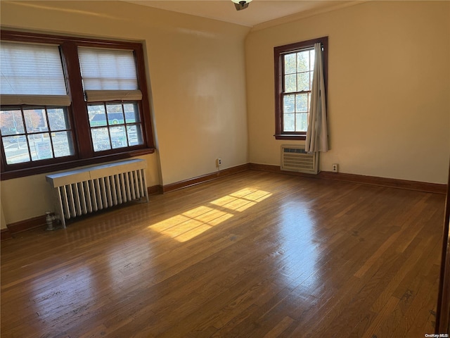 empty room with wood-type flooring, radiator heating unit, and a wall unit AC