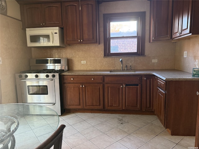 kitchen featuring backsplash, sink, light tile patterned floors, and stainless steel gas range