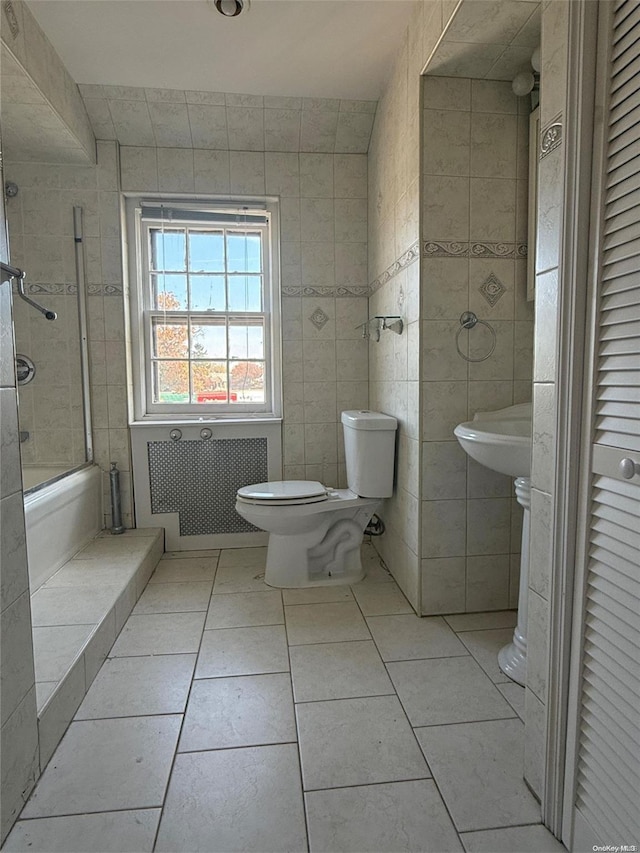 bathroom featuring tile patterned floors, radiator, tile walls, toilet, and tiled shower / bath