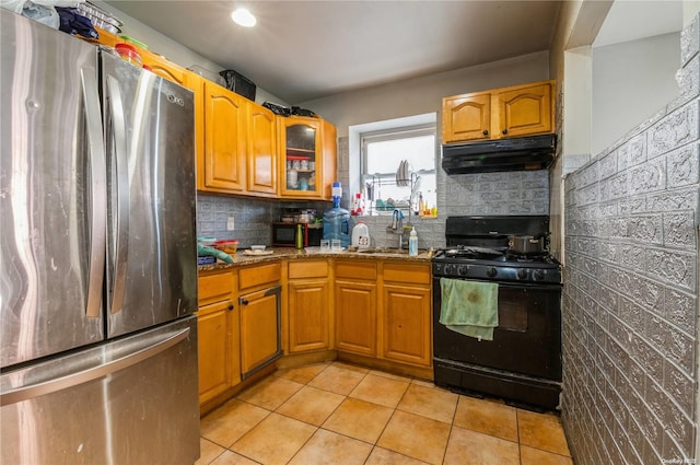 kitchen featuring stainless steel fridge, light stone counters, black gas range oven, sink, and light tile patterned flooring