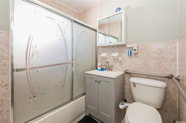 full bathroom featuring combined bath / shower with glass door, vanity, toilet, and tile walls