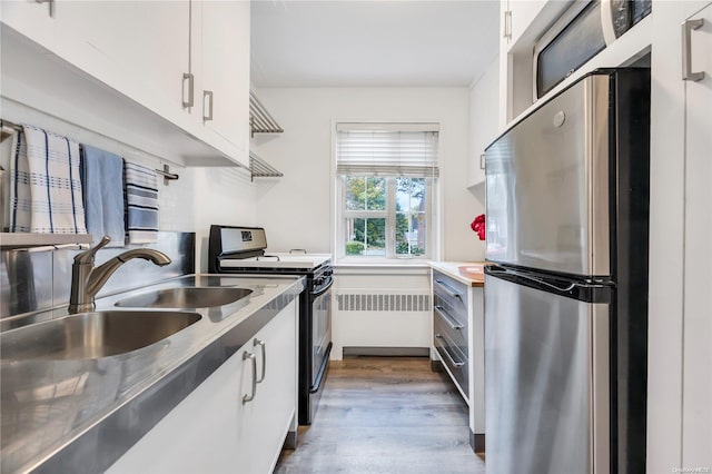 kitchen with stainless steel appliances, sink, radiator heating unit, dark hardwood / wood-style floors, and white cabinetry