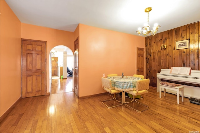 dining room featuring a chandelier, light hardwood / wood-style floors, and wooden walls