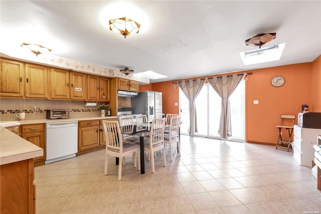 kitchen with dishwasher, a skylight, tasteful backsplash, light tile patterned flooring, and stainless steel fridge with ice dispenser