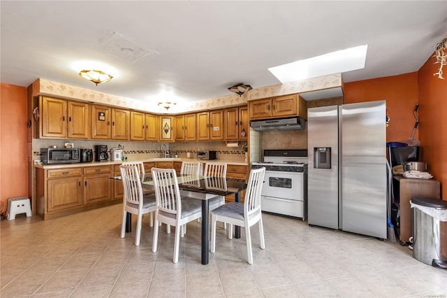 kitchen with backsplash, sink, a skylight, light tile patterned floors, and stainless steel appliances