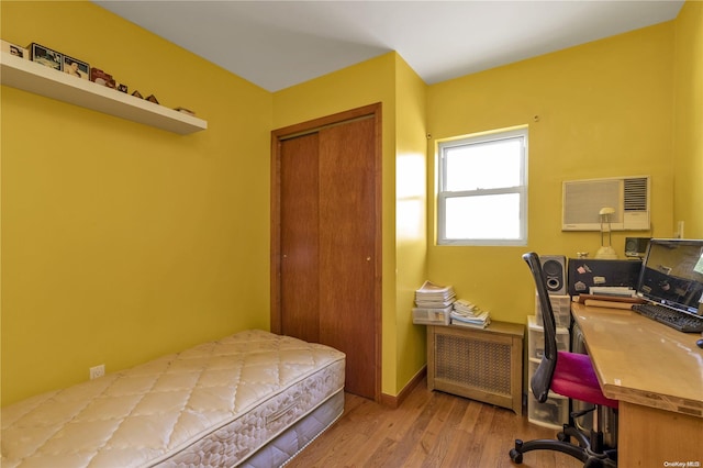 bedroom with light hardwood / wood-style floors, a wall unit AC, radiator, and a closet