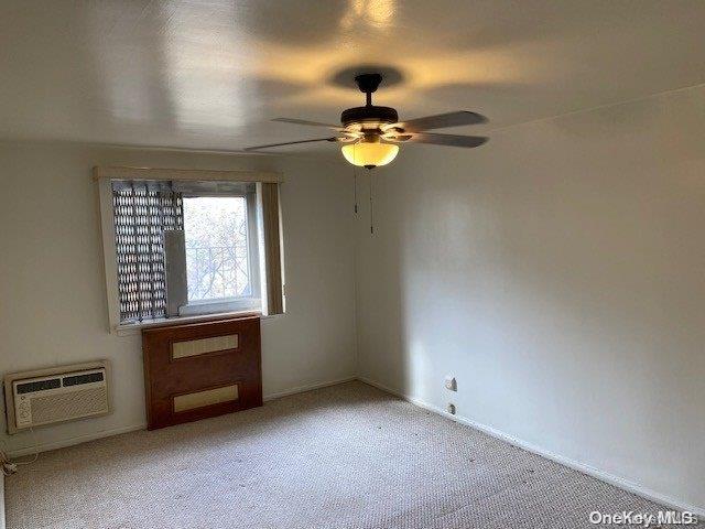 empty room featuring light carpet, ceiling fan, and a wall mounted air conditioner