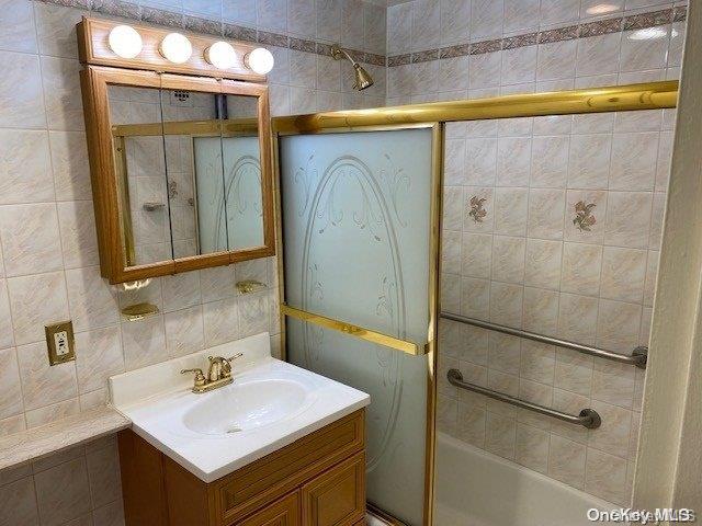 bathroom with vanity, shower / bath combination with glass door, and tile walls