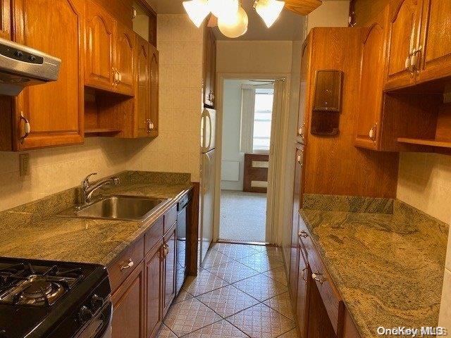 kitchen with black gas range oven, ventilation hood, sink, dark stone countertops, and dishwasher