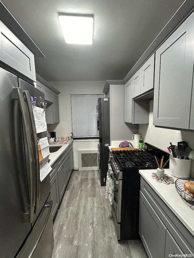 kitchen with gray cabinetry, light wood-type flooring, and stainless steel appliances