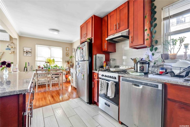 kitchen featuring stainless steel appliances, light stone counters, backsplash, light wood-type flooring, and ornamental molding