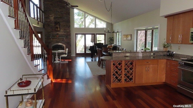 kitchen with dark hardwood / wood-style flooring, ceiling fan with notable chandelier, high vaulted ceiling, stainless steel range oven, and a fireplace