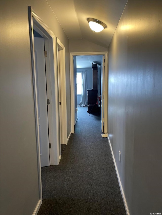 hall with vaulted ceiling and dark colored carpet