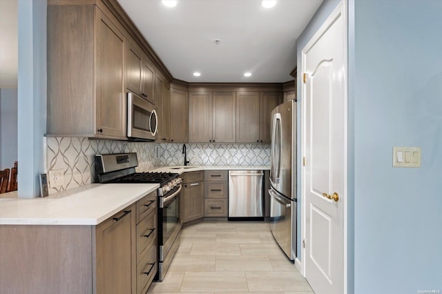 kitchen featuring sink, tasteful backsplash, light stone counters, kitchen peninsula, and appliances with stainless steel finishes