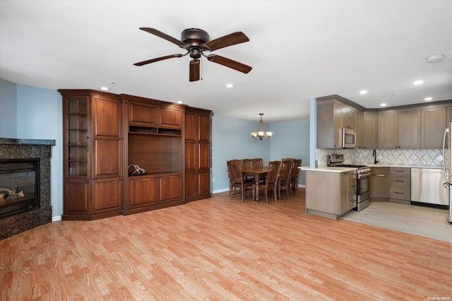 kitchen featuring appliances with stainless steel finishes, backsplash, pendant lighting, a fireplace, and light hardwood / wood-style floors