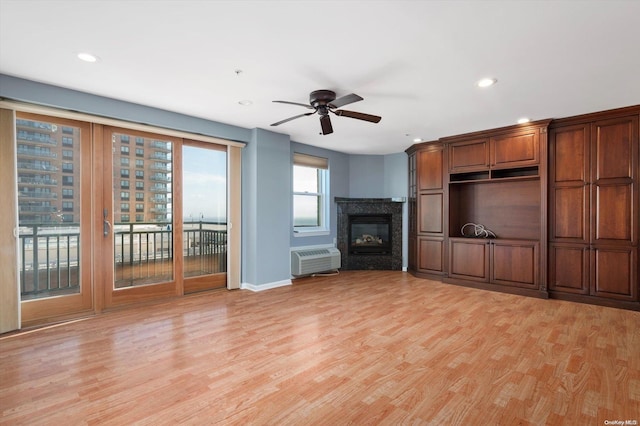 unfurnished living room with an AC wall unit, ceiling fan, a fireplace, and light wood-type flooring