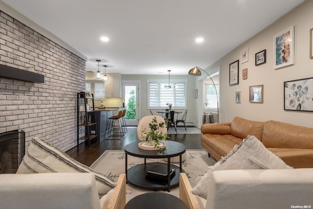 living room with a chandelier, dark hardwood / wood-style flooring, a brick fireplace, and brick wall