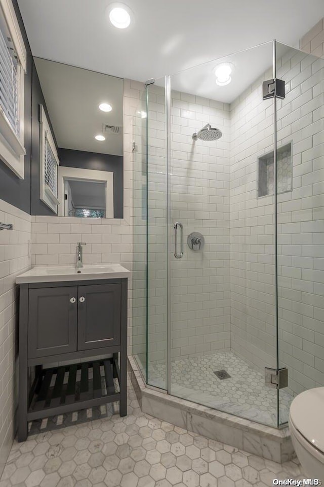 bathroom with tile patterned floors, toilet, vanity, a shower with shower door, and tile walls