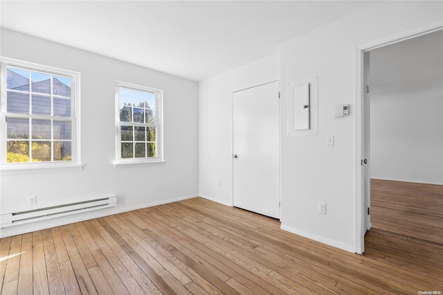 unfurnished bedroom featuring baseboard heating, electric panel, and light hardwood / wood-style flooring