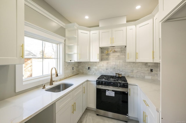 kitchen with sink, backsplash, light stone counters, gas range oven, and white cabinets