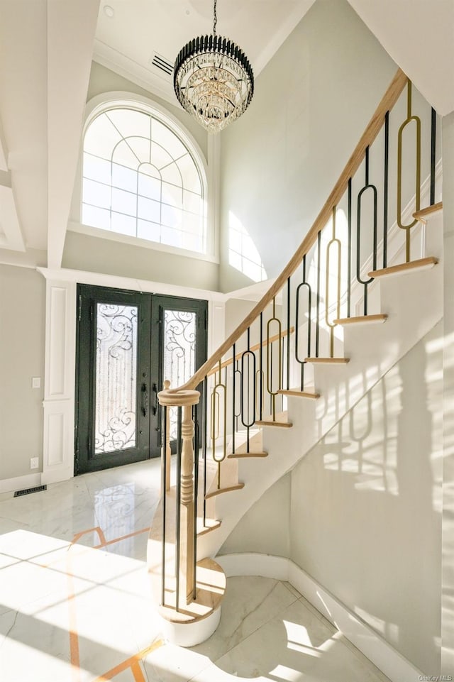 foyer with crown molding, an inviting chandelier, french doors, and a towering ceiling