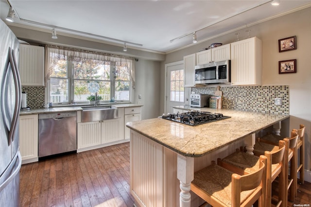 107 Jessup Ave, Quogue, NY 11959 - kitchen with stainless steel appliances, rail lighting, a peninsula, backsplash, and a breakfast bar