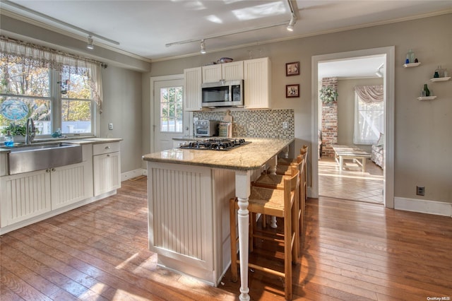 kitchen with rail lighting, light hardwood / wood-style flooring, a breakfast bar area, appliances with stainless steel finishes, and ornamental molding