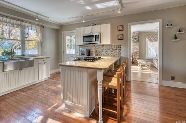 107 Jessup Ave, Quogue, NY 11959 - kitchen featuring stainless steel microwave, track lighting, a sink, ornamental molding, and hardwood / wood-style flooring