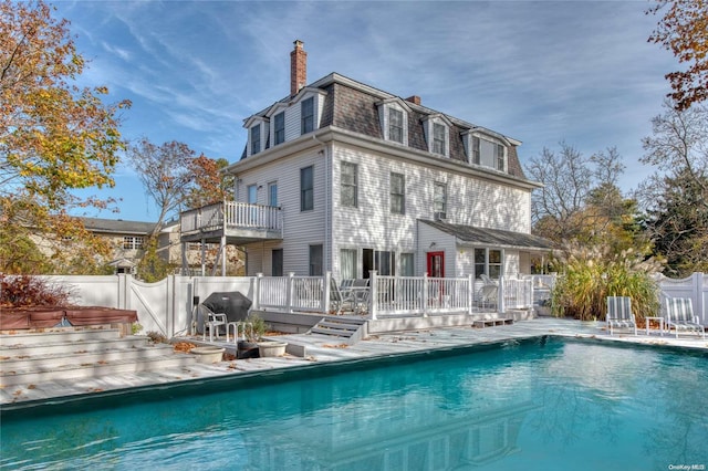 back of property featuring a swimming pool with hot tub and a balcony