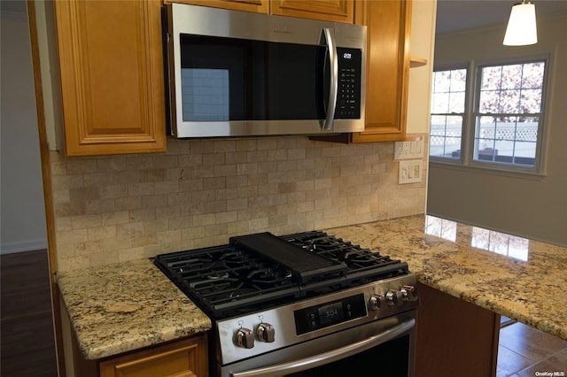 kitchen featuring backsplash, crown molding, light stone countertops, appliances with stainless steel finishes, and decorative light fixtures