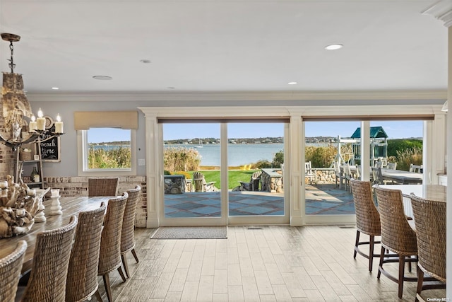 dining room featuring a water view, light wood-type flooring, a notable chandelier, and ornamental molding