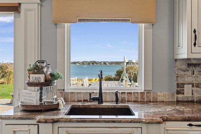 kitchen featuring white cabinets, dark stone counters, decorative backsplash, sink, and a water view
