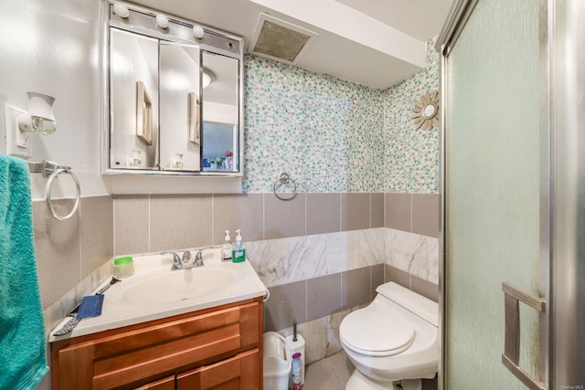 bathroom with vanity, a shower with shower door, tile walls, and toilet