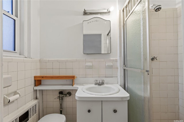 bathroom with a tile shower, radiator, vanity, and tile walls