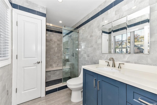 bathroom featuring vanity, toilet, a shower with door, and tile walls