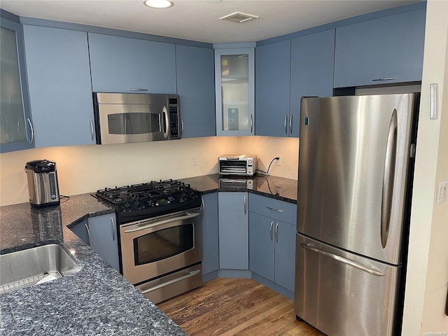 kitchen with dark stone counters, stainless steel appliances, blue cabinets, and dark wood-type flooring