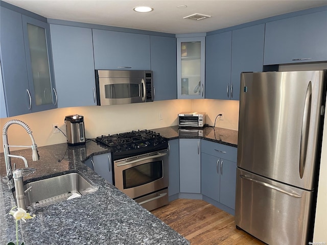 kitchen with blue cabinetry, dark stone countertops, and stainless steel appliances