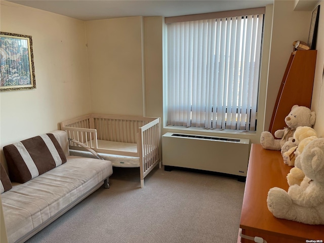 bedroom with a crib, light colored carpet, and radiator