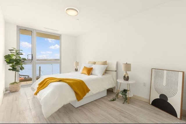 bedroom featuring light wood-type flooring, a water view, and floor to ceiling windows