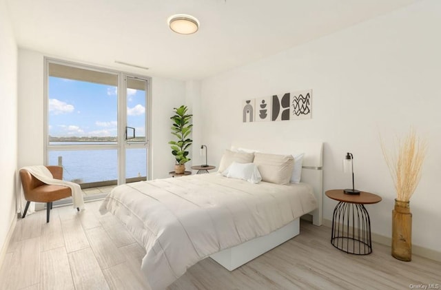 bedroom with light hardwood / wood-style floors and a water view