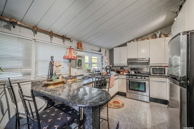 kitchen featuring kitchen peninsula, appliances with stainless steel finishes, a kitchen breakfast bar, vaulted ceiling, and white cabinets