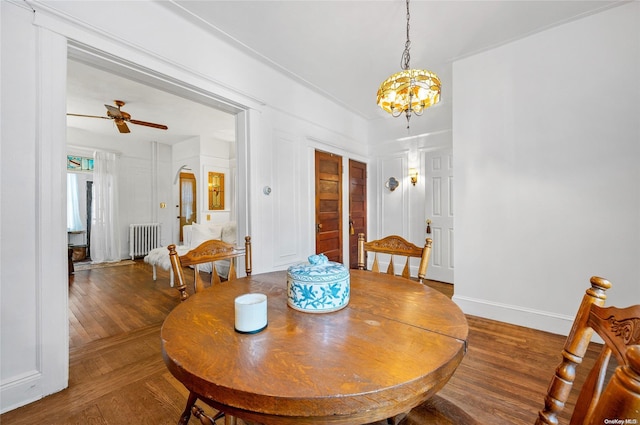 dining space featuring hardwood / wood-style flooring, ceiling fan with notable chandelier, and radiator