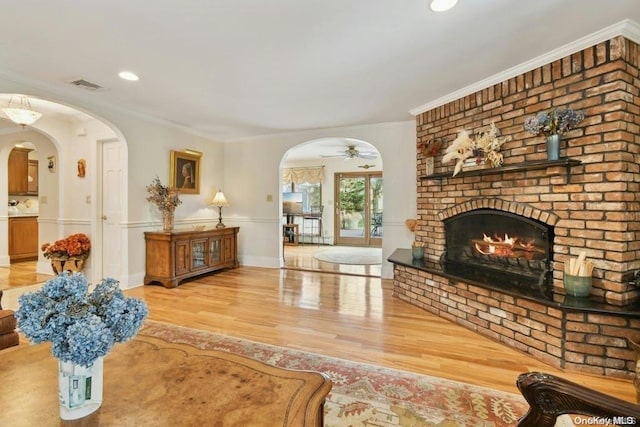 living room featuring crown molding, a fireplace, ceiling fan, and light wood-type flooring