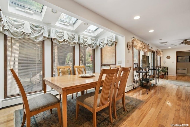 dining area featuring a skylight, ceiling fan, a baseboard heating unit, radiator heating unit, and light hardwood / wood-style floors