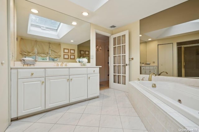 bathroom featuring tile patterned floors, vanity, tiled bath, and a skylight