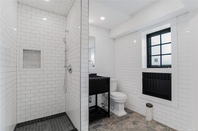 bathroom with a tile shower, heating unit, tile walls, and toilet