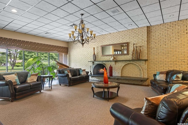 carpeted living room featuring a paneled ceiling, a brick fireplace, a notable chandelier, and brick wall